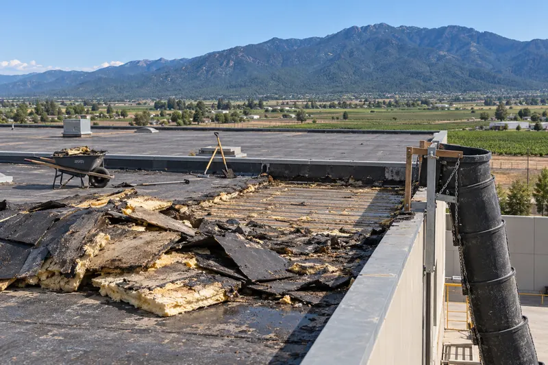 Torn-off roofing and wet insulation piled by a debris chute at the roof edge
